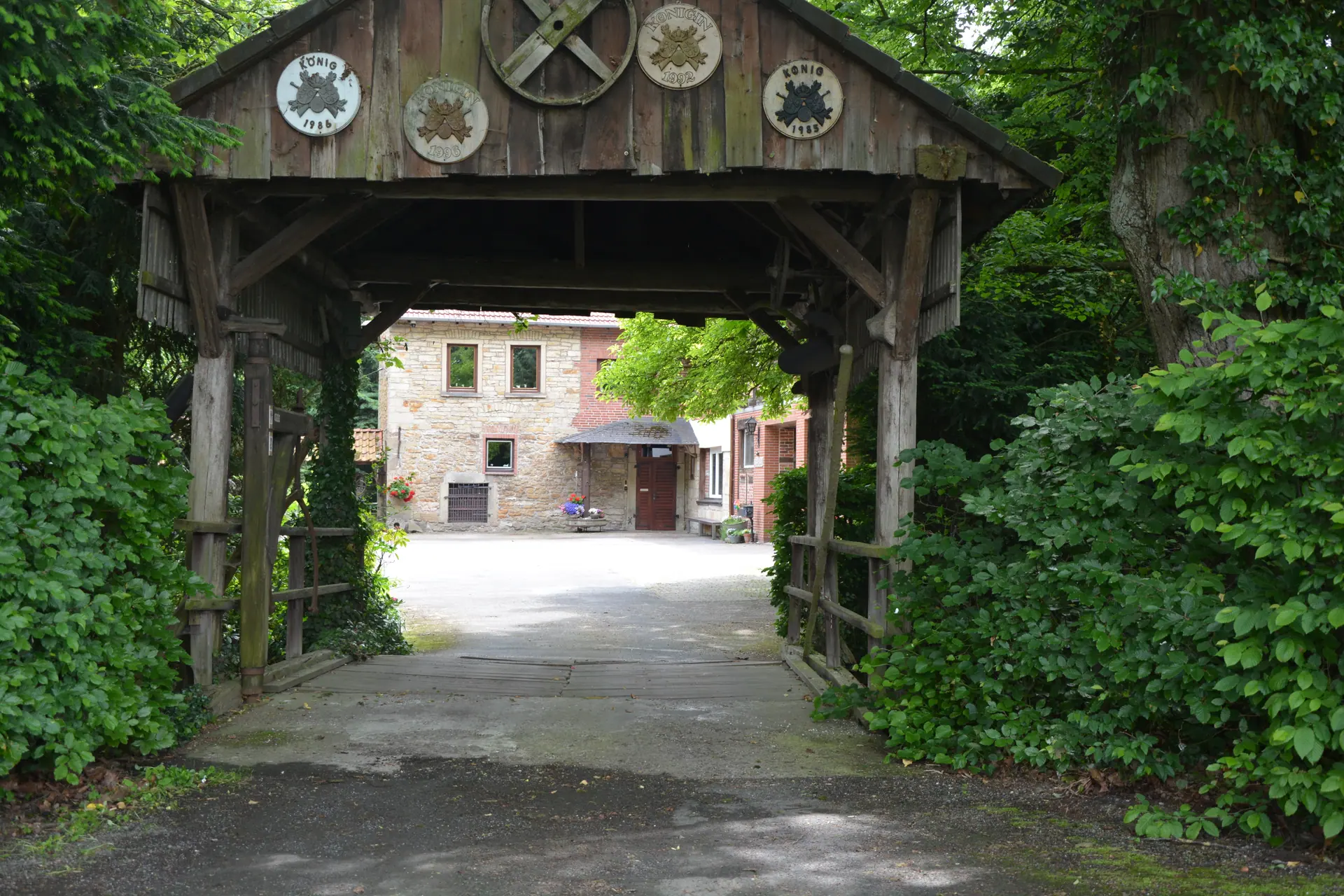 Blick durch die überdachte Holzbrücke auf den Mühlenhof – hier biegen Sie ein