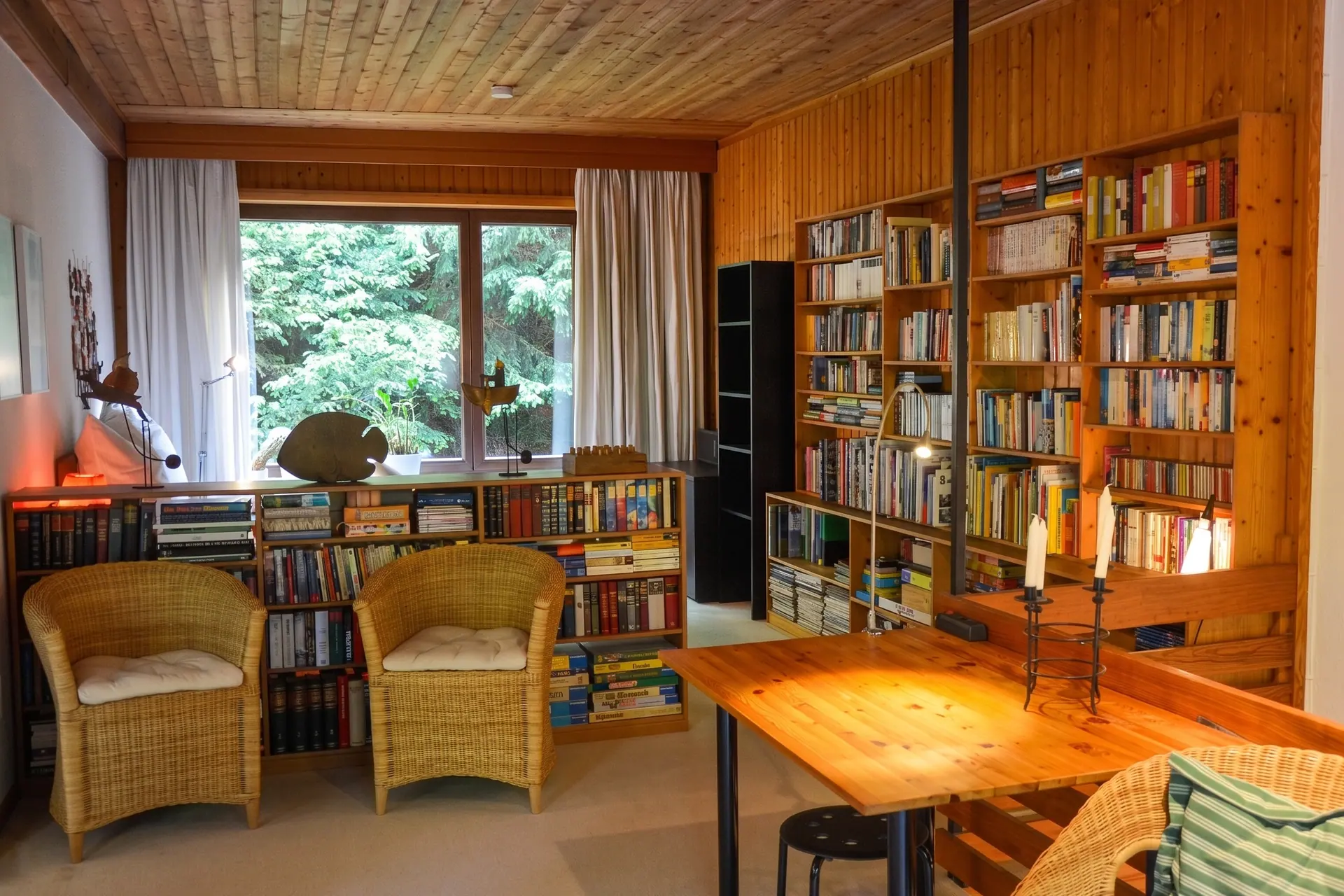 Wohnzimmer mit Bibliothek, Korbsesseln und großem Fenster ins Grüne